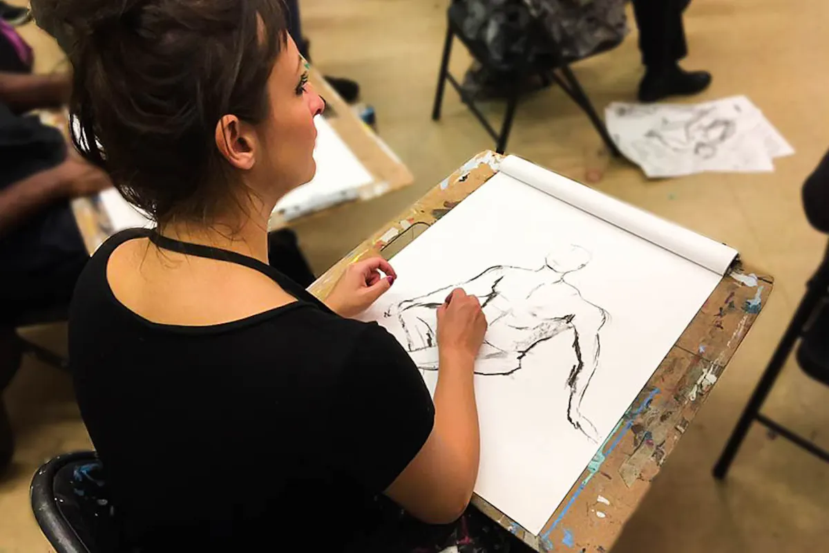 A participant drawing a figure on a sketchpad in an art studio
