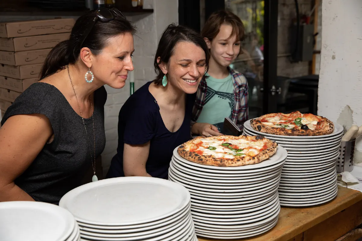 Visitors leaning toward freshly baked pizzas during a Brooklyn pizza outing